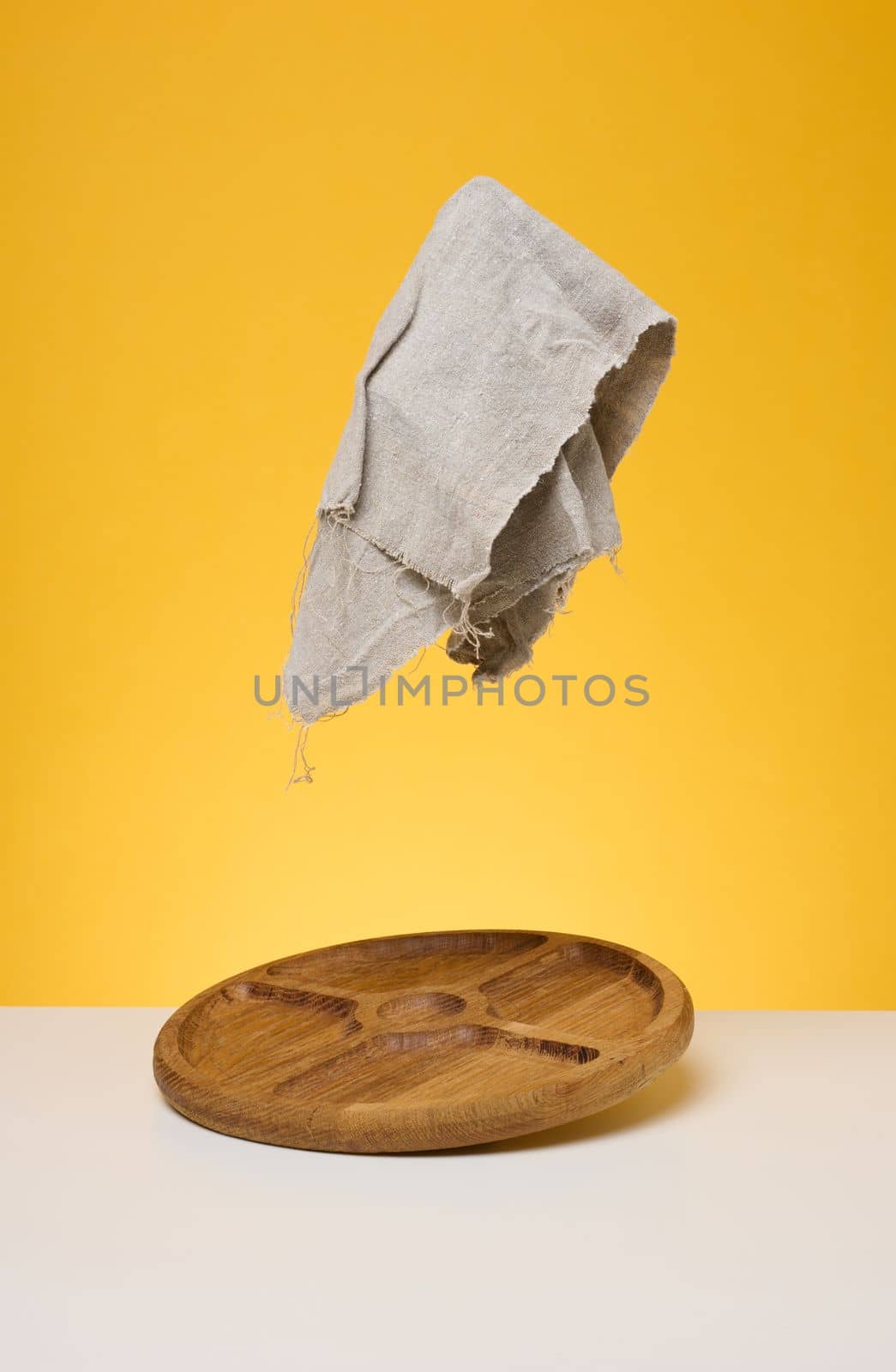 Round wooden board and gray napkin on yellow background by ndanko