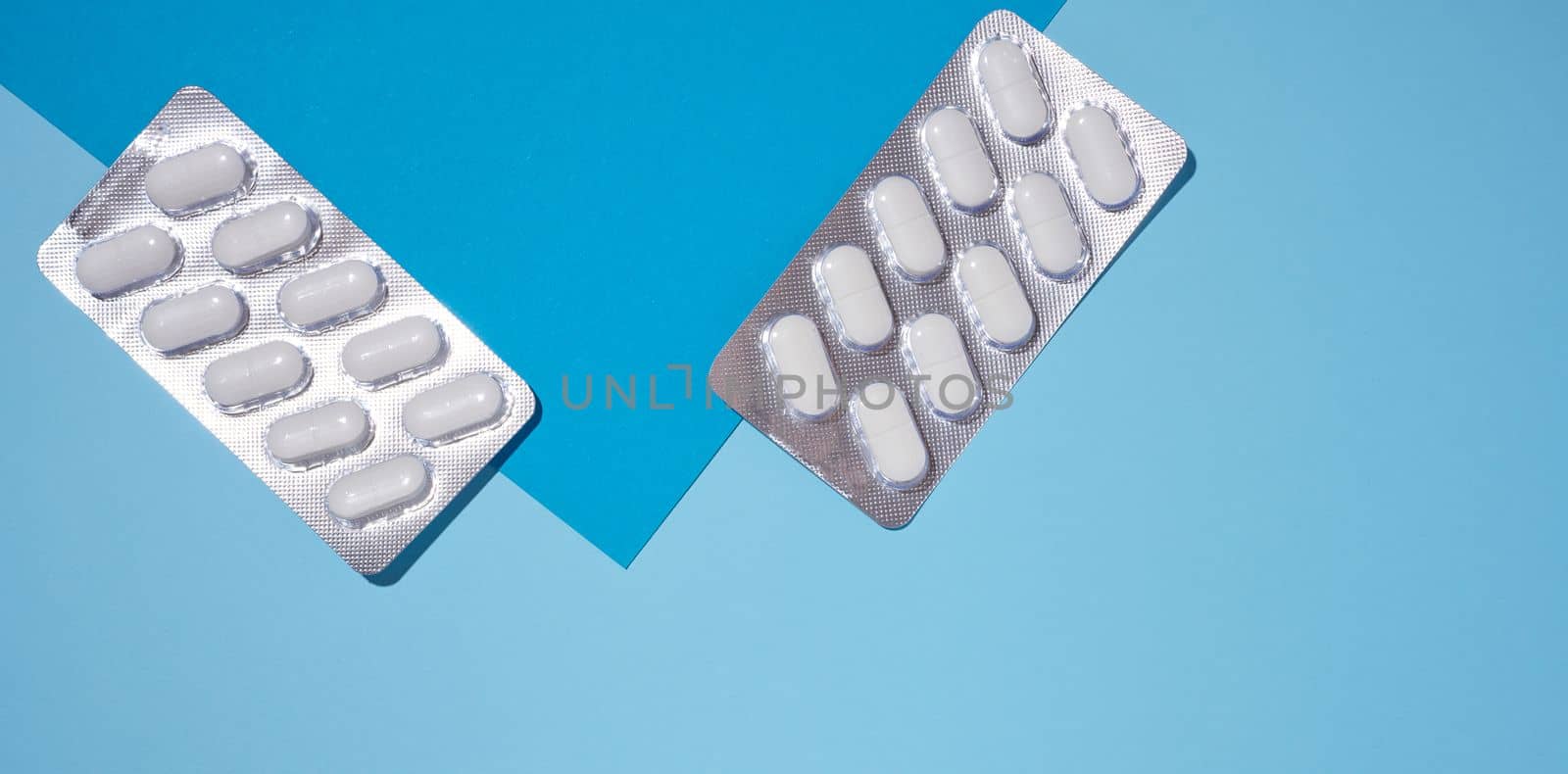 Oval white pills in a gray blister pack on a blue background, top view. Copy space