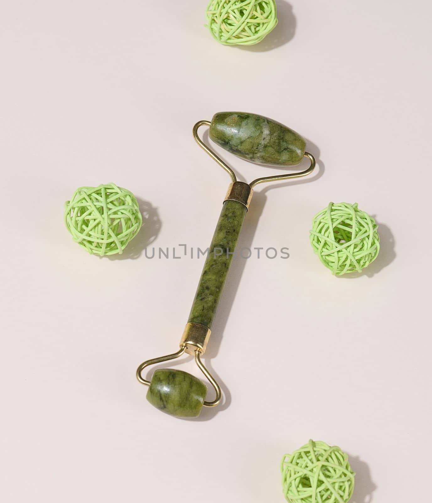 Jade green face massager on a beige background, top view