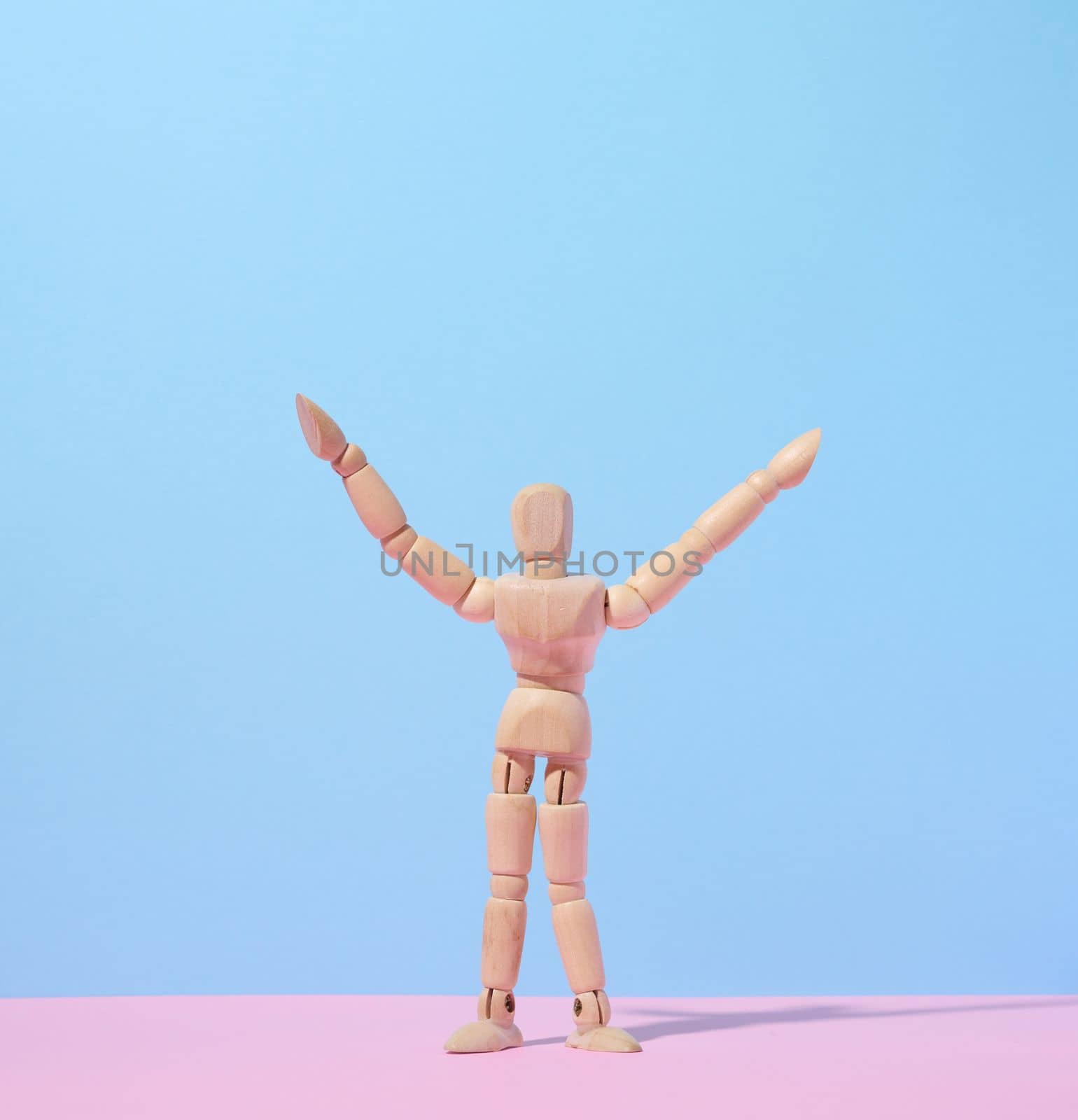 Wooden puppet man on a blue background, arms raised up by ndanko