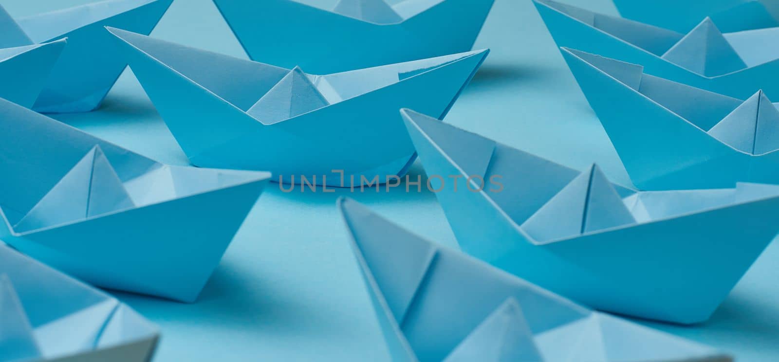 A group of blue paper boats on a blue background. The concept of a controlled crowd, the influence of a leader