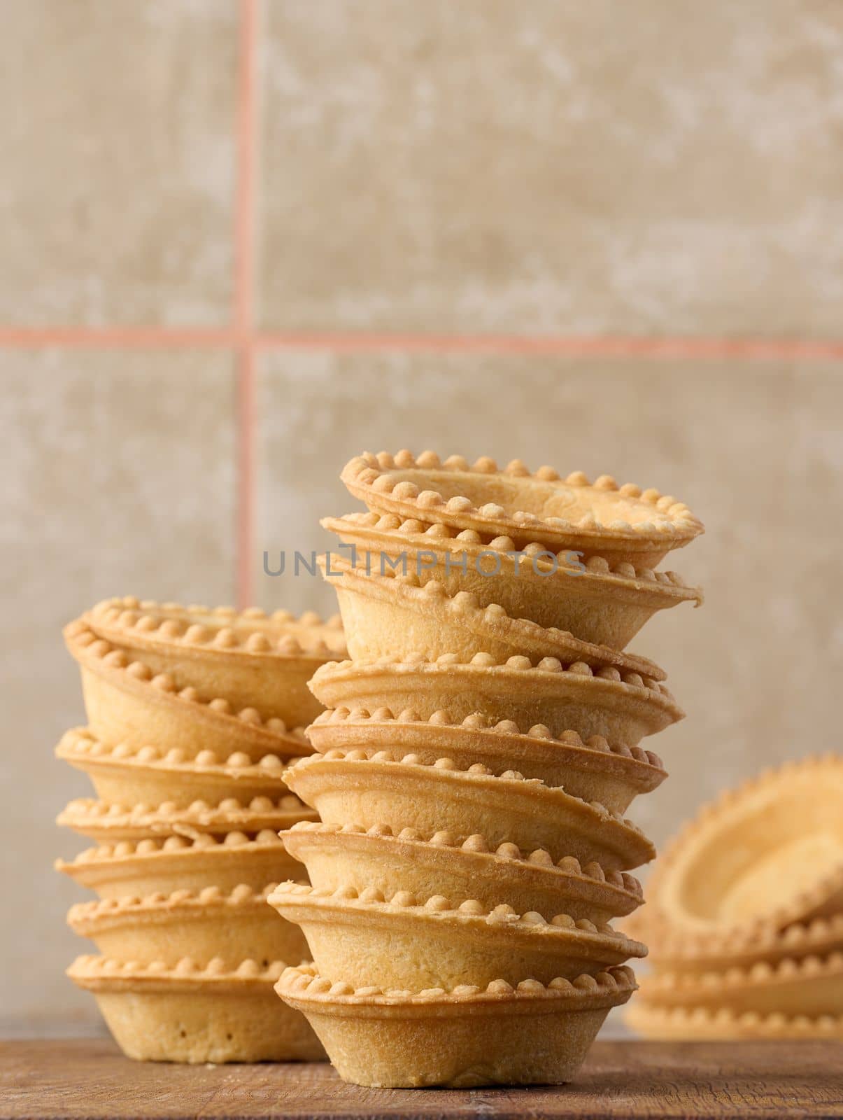 Stack of empty baked round canape baskets on a wooden board, round empty tartlets