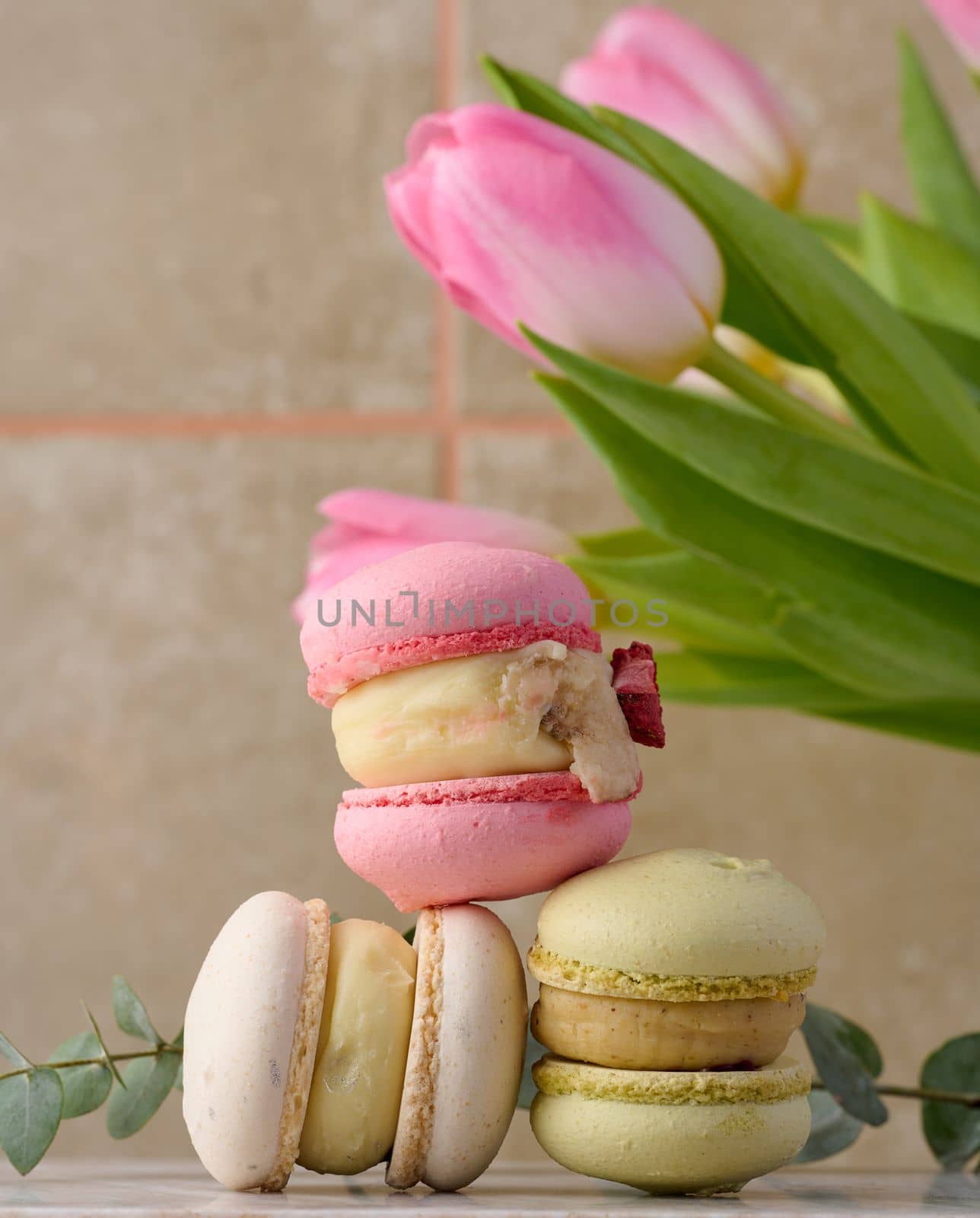 Baked macarons with different flavors on the table, behind a bouquet of tulips by ndanko