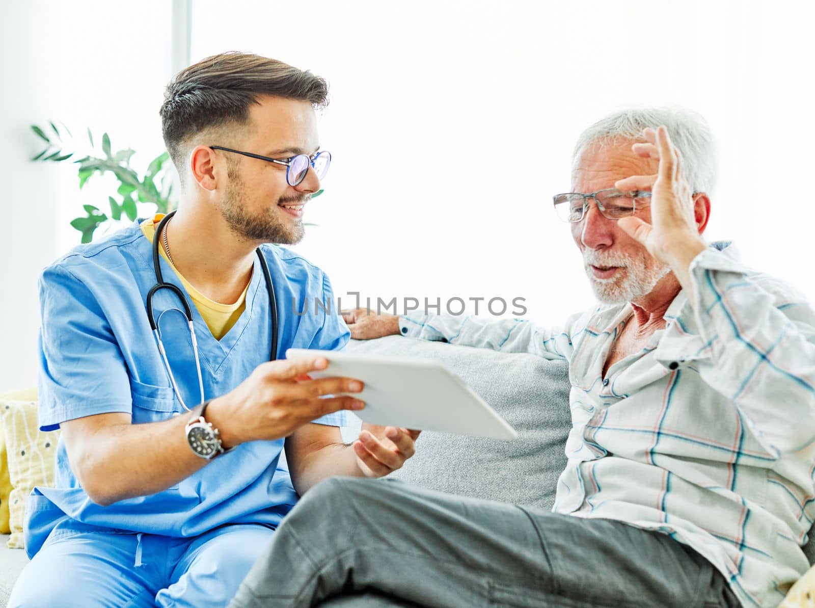 Doctor or nurse caregiver showing a tablet screen to senior man at home or nursing home