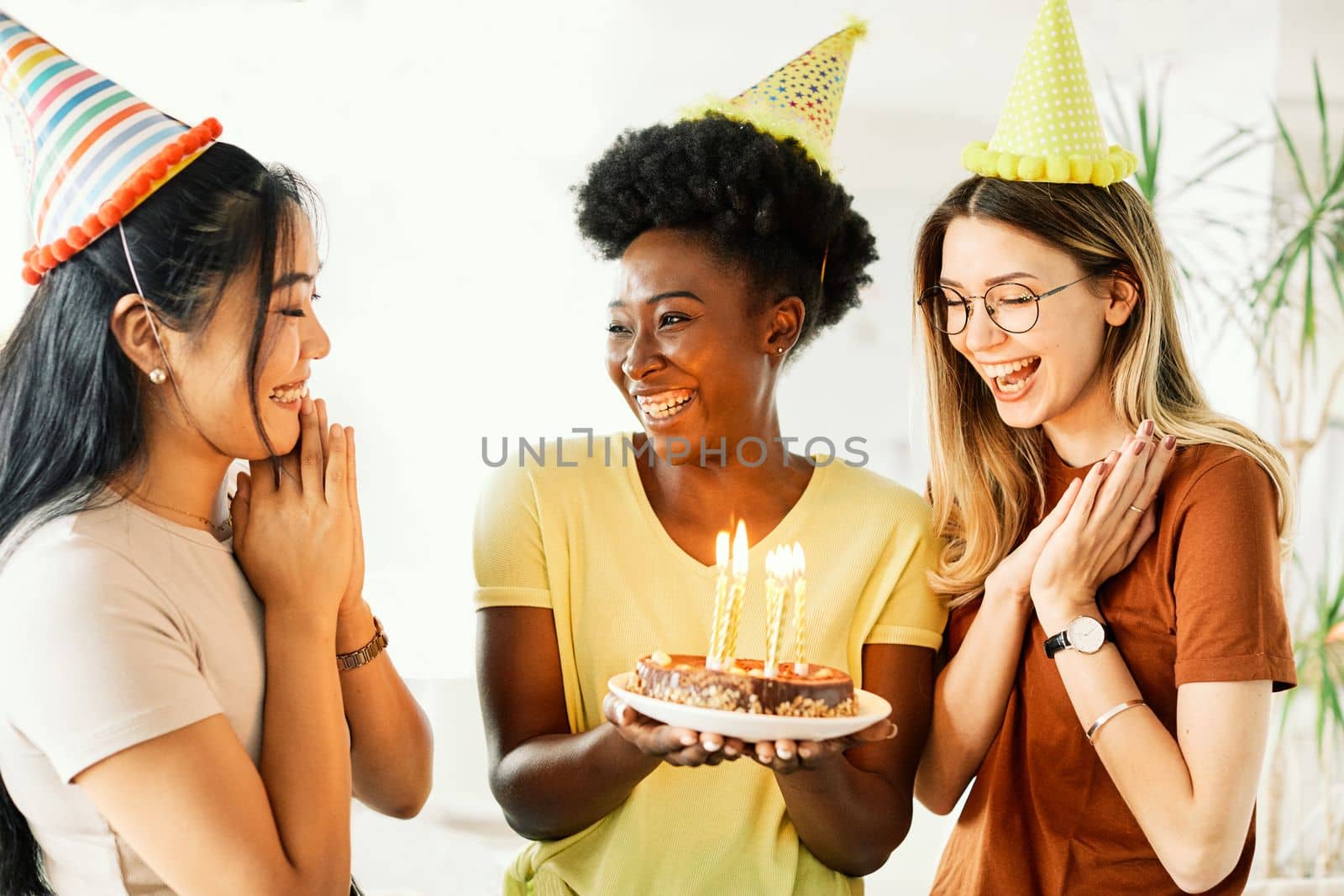 Group of young happy people friends having fun blowing candles on a birthday cake at home