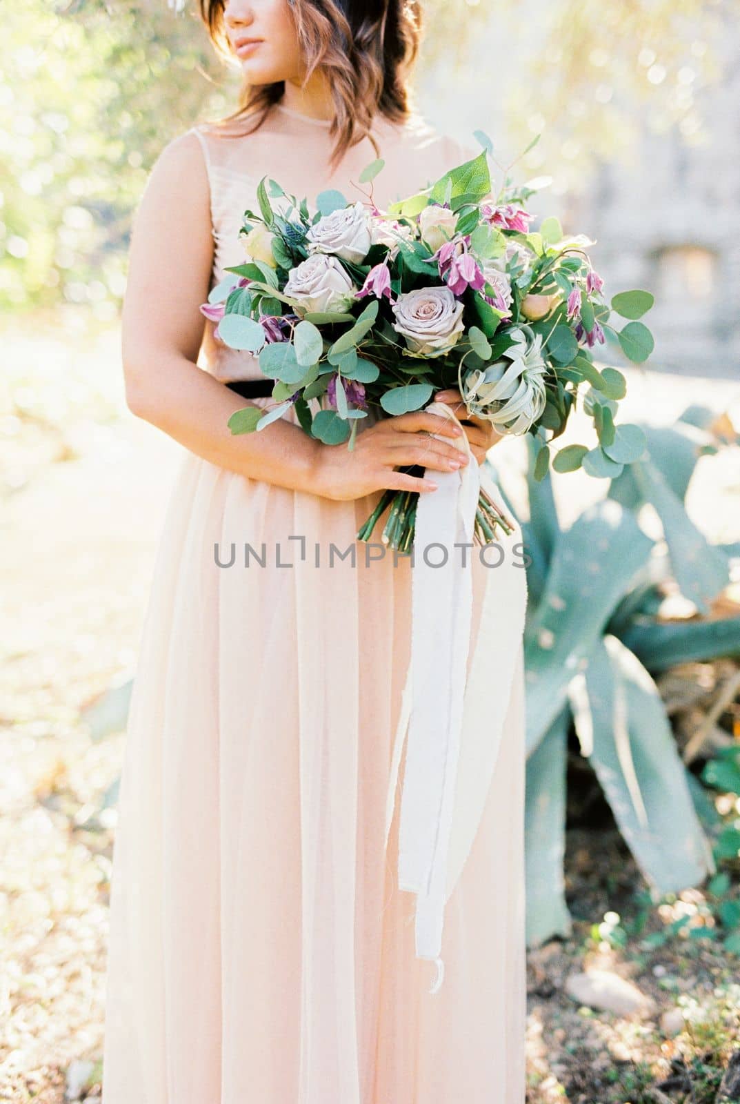 Bouquet of flowers in the hands of the bride standing near the tree. High quality photo