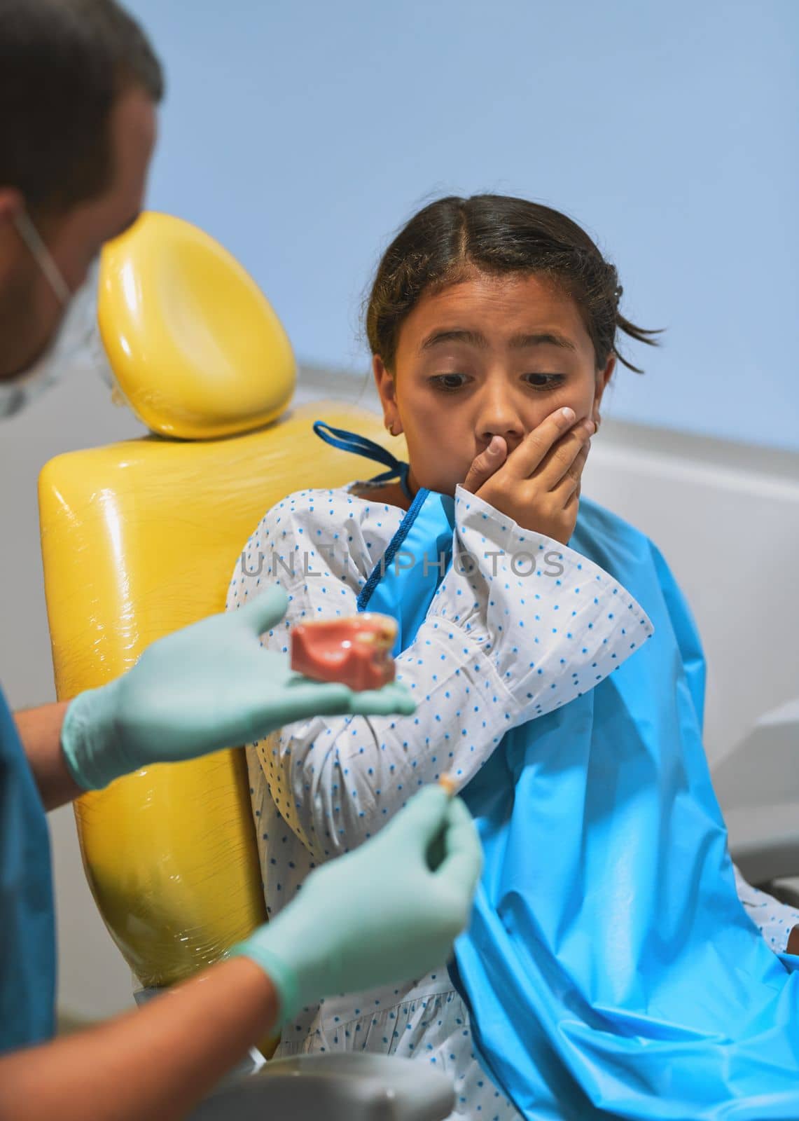 Wow I never knew it looks like that. a surprised looking little girl holding her mouth closed while looking at a tooth that the dentist just pulled out
