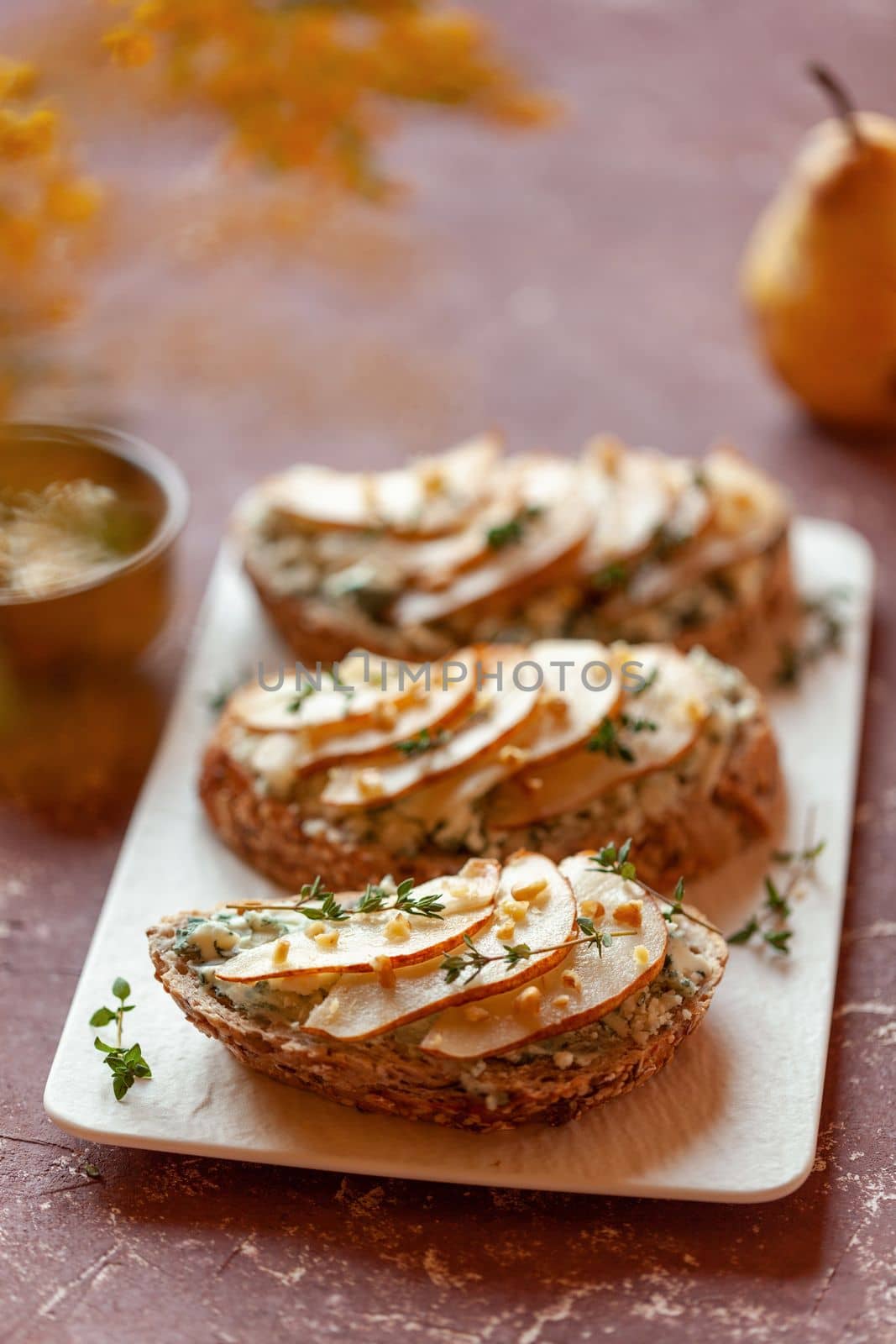 roquefort french cheese and sliced peaches toasts on a square plate, on a table under mimosa flowers