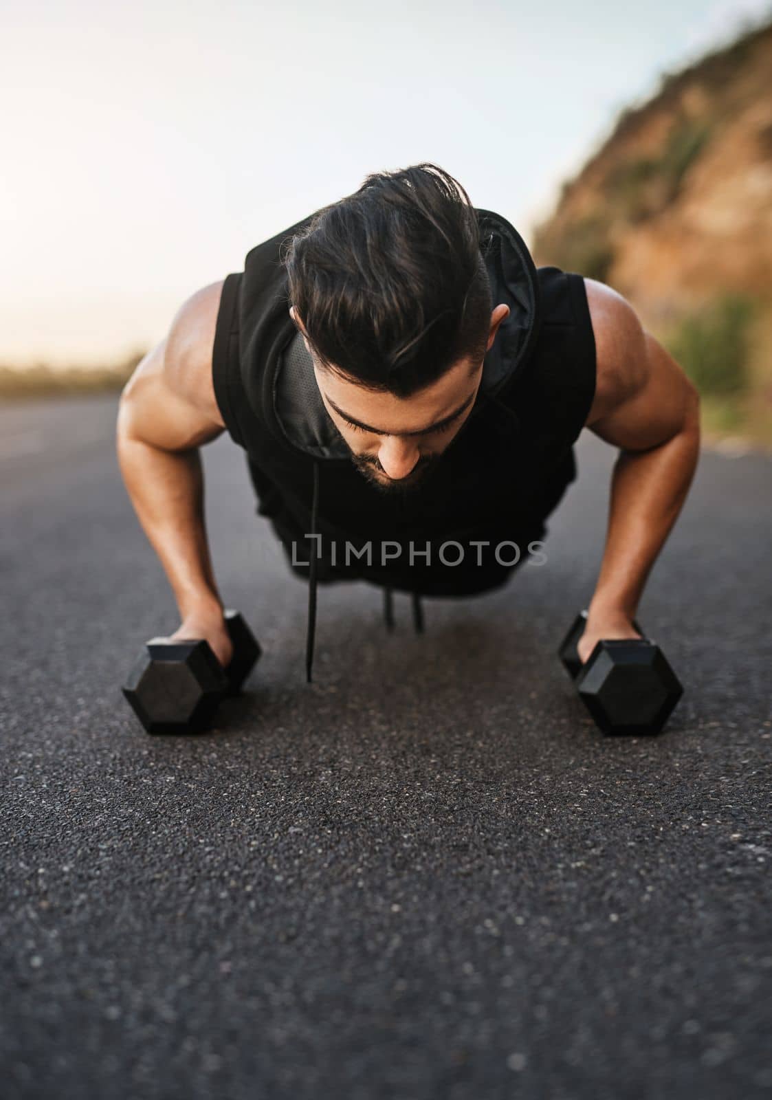 Its time to boost this workout. a sporty young man exercising with weights outdoors. by YuriArcurs