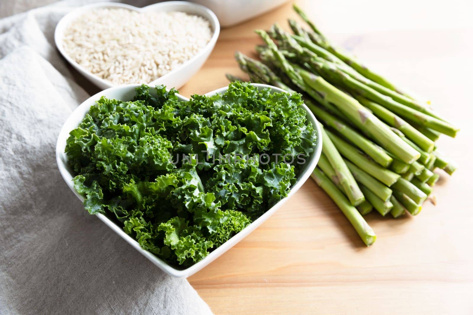 Healthy kale in a heart shaped bowl with asparagus and rice, raw ingredients