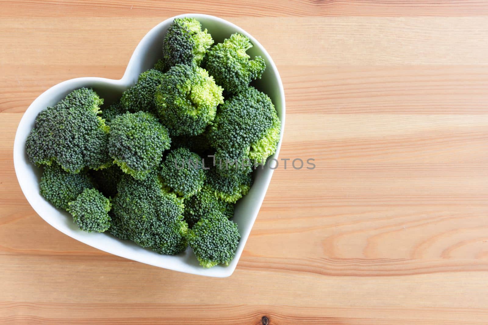 Flat lay of fresh raw broccoli in a heart shaped bowl with copy space.
