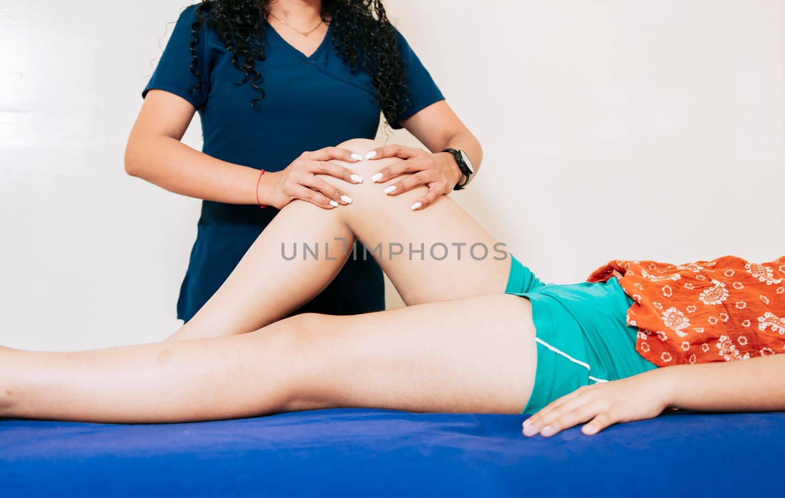 Knee rehabilitation physiotherapy to patient lying down. Female physiotherapist checking knee to female patient. Physiotherapist hands checking knee of female patient by isaiphoto