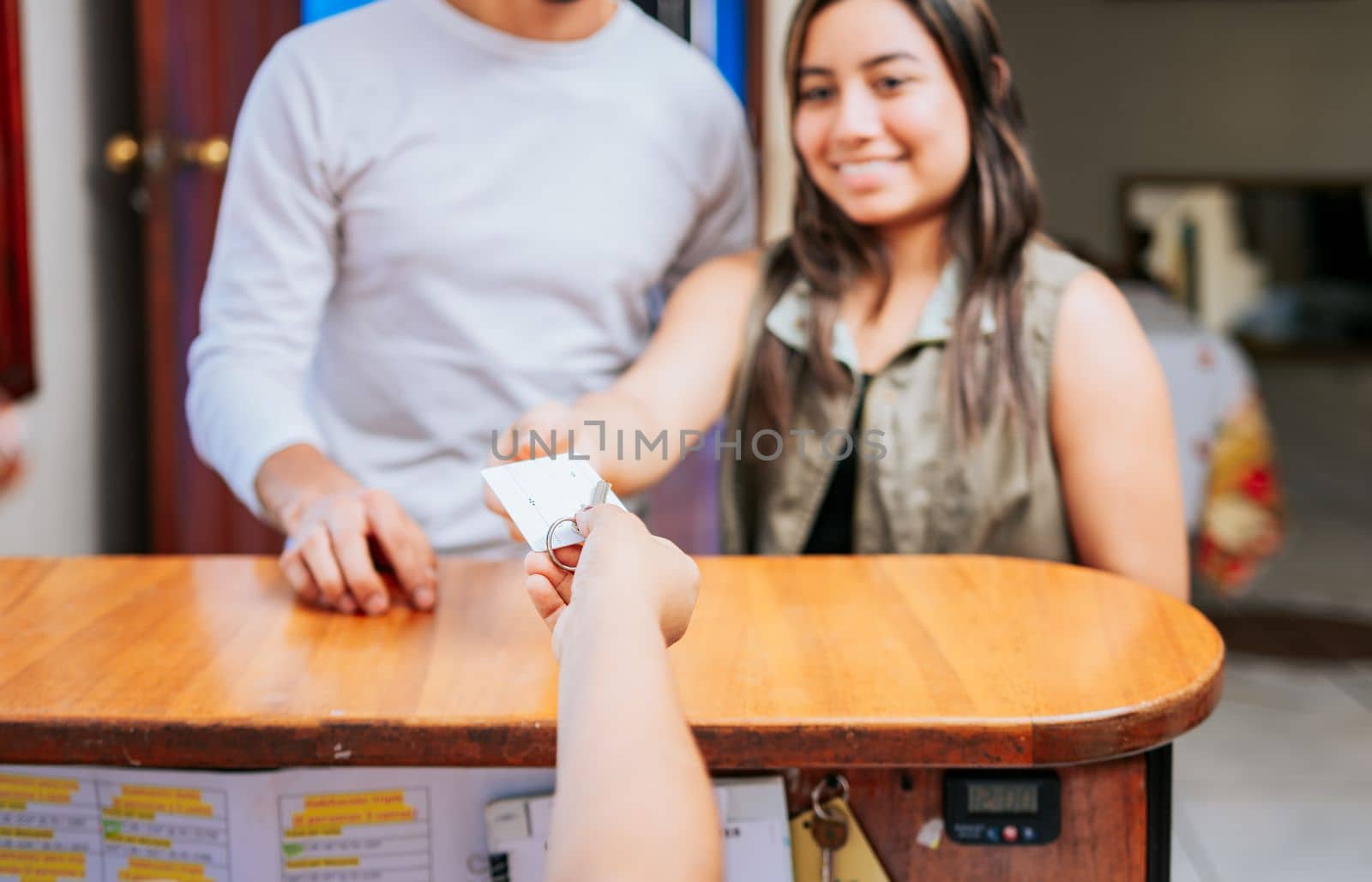 Receptionist giving hotel room keys to couple. Hand giving hotel room key to couple. Latin couple receiving hotel room keys. Concept of couple arriving at hotel