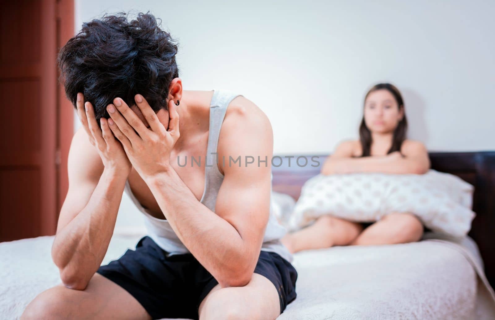 Worried man sitting on the side of the bed and angry wife. Worried man in bed with erectile dysfunction. Concept of crisis and couple problems in bed
