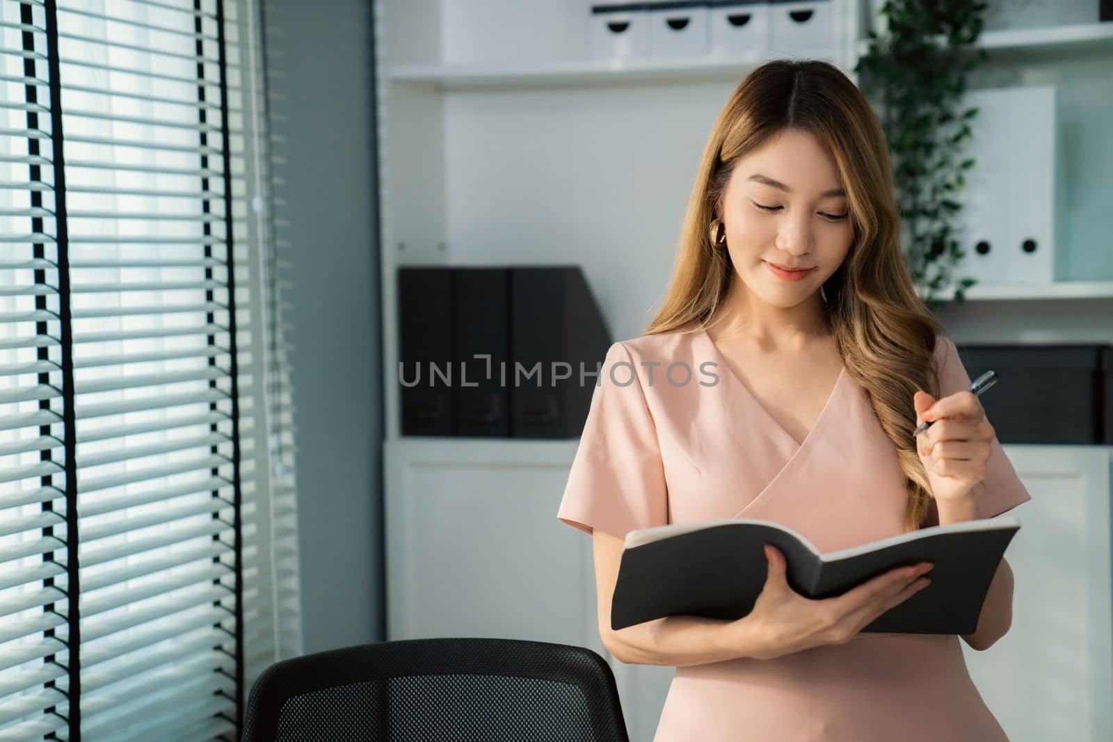 Young competent office lady, intern, secretary holding a log in office room. by biancoblue