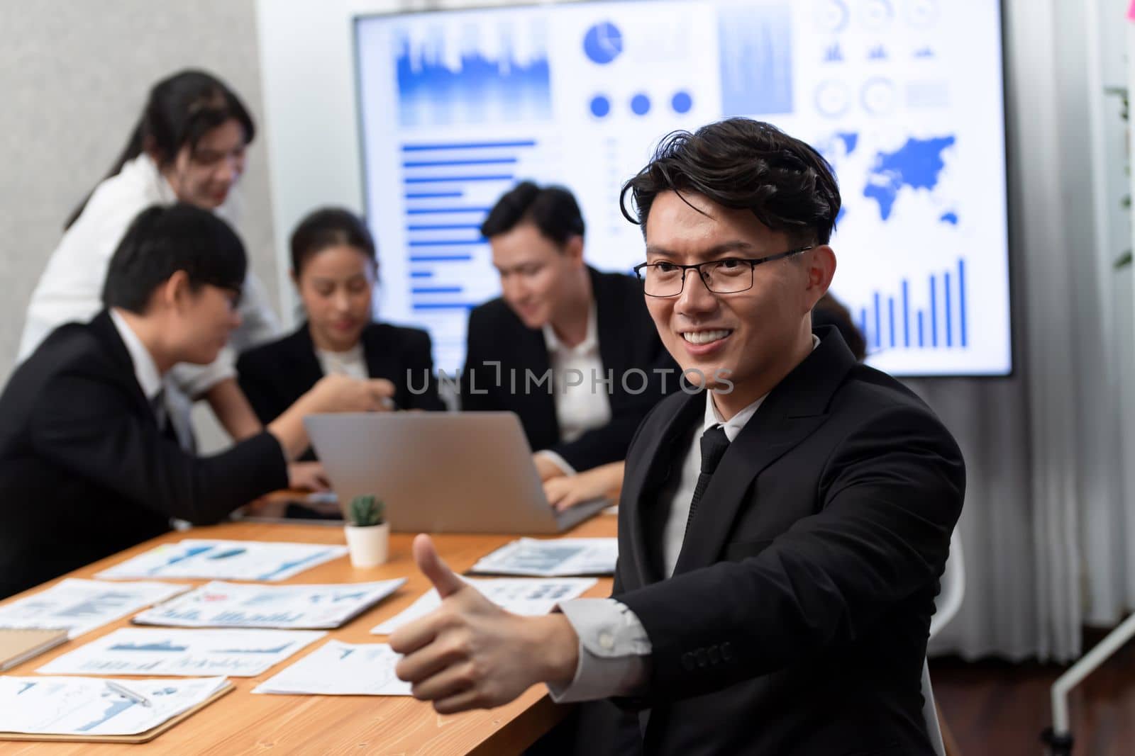 Focus portrait of successful confident male manager or executive in business wear with blurred background of businesspeople, colleagues working with financial report papers in office of harmony.