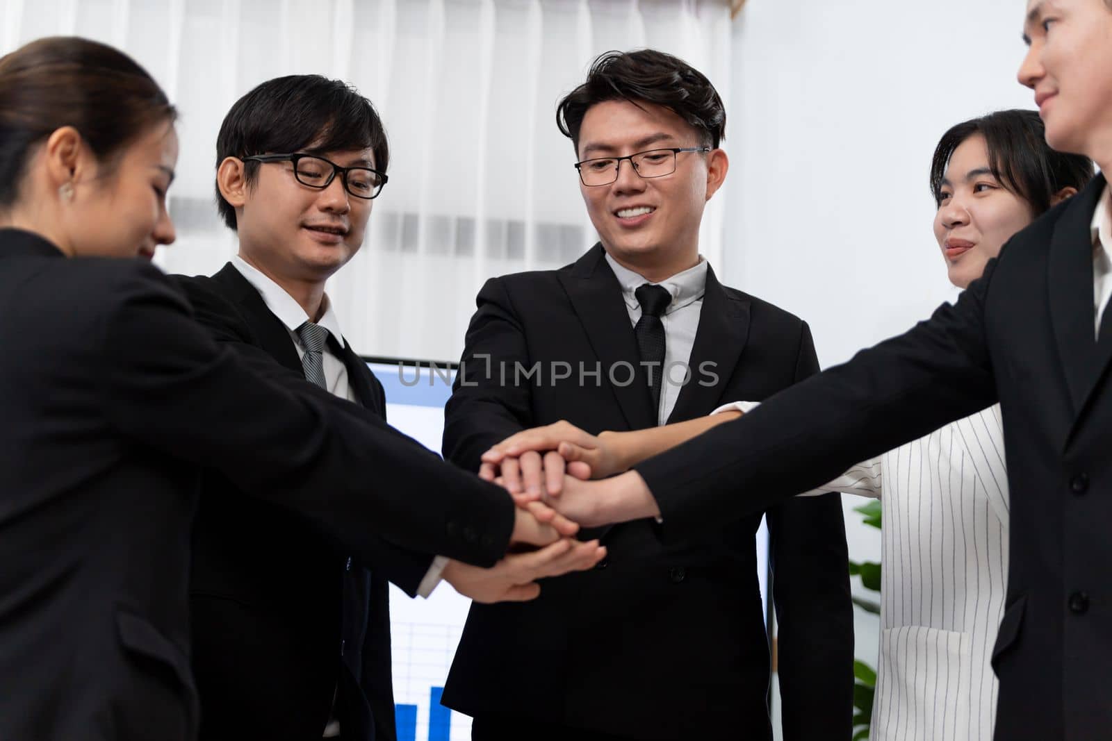 Closeup business team of suit-clad businessmen and women join hand stack together and form circle. Colleague collaborate and work together to promote harmony and teamwork concept in office workplace.