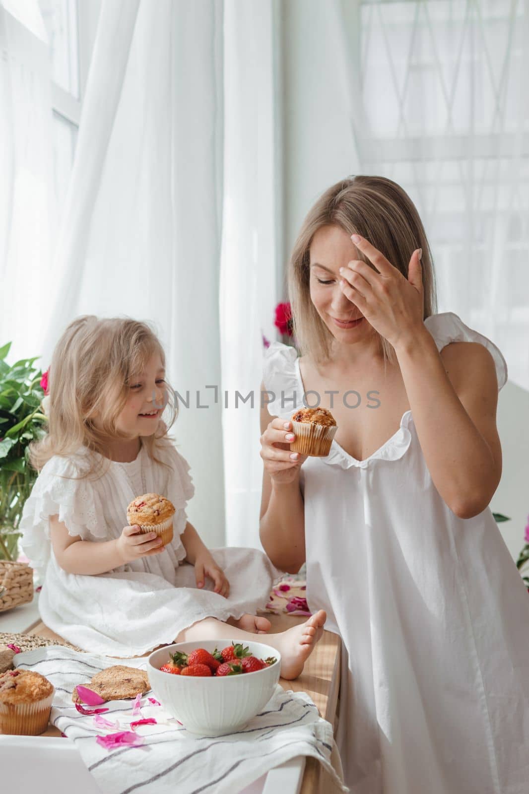 A little blonde girl with her mom on a kitchen countertop decorated with peonies. The concept of the relationship between mother and daughter. Spring atmosphere.