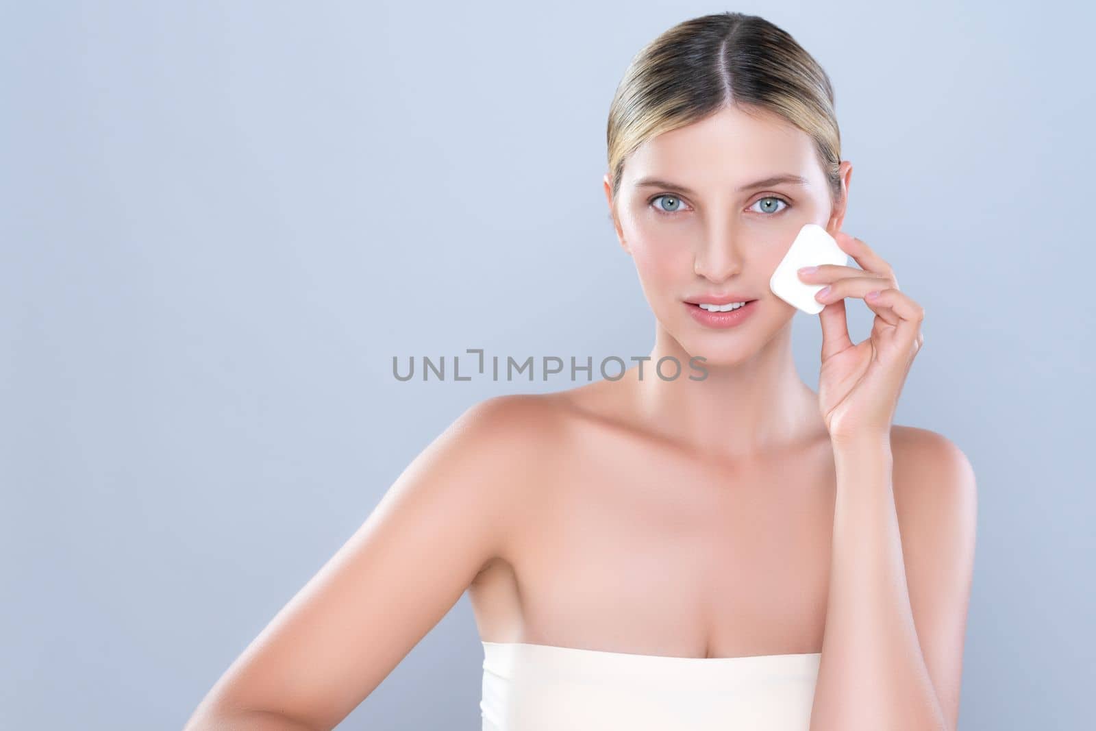 Alluring beautiful female model applying powder puff for facial makeup concept. Portrait of flawless perfect cosmetic skin woman put powder foundation on her face in isolated background.