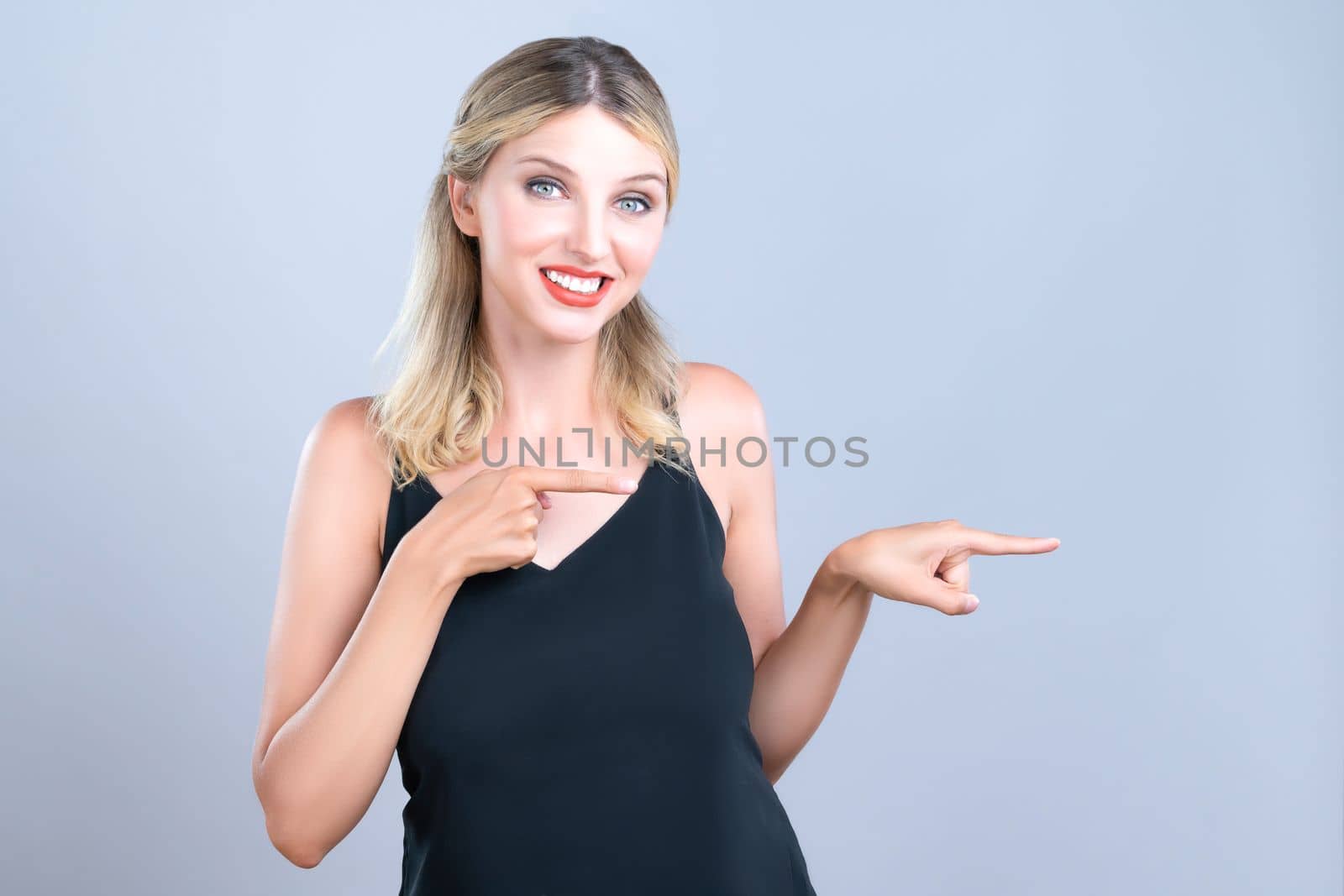 Alluring portrait of beautiful woman with perfect makeup clean skin pointing finger side way in copyspace isolated background. Promotion indicated by hand gesture concept for skincare advertisement.