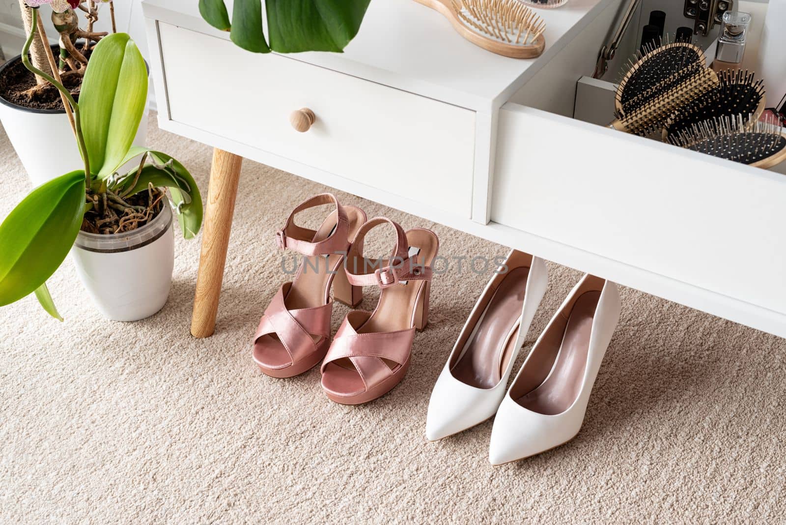 Stylish light room interior with elegant vanity table and plants, beauty and fashion. closeup of elegant high heel shoes standing under feminine dressing table