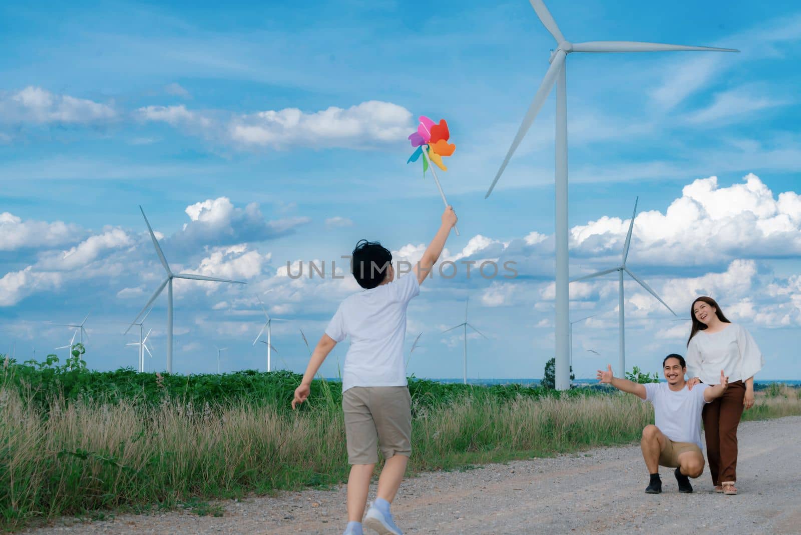 Progressive happy family enjoying their time at wind farm for green energy production concept. Wind turbine generators provide clean renewable energy for eco-friendly purposes.