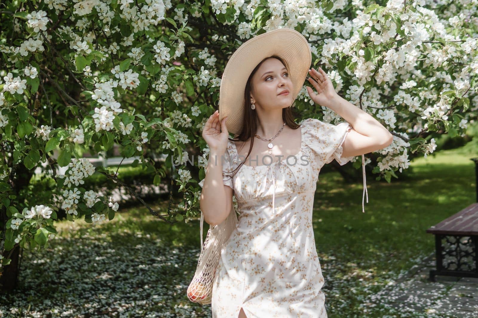 An attractive long-haired woman walks in the spring in the park of blooming apple trees. Spring portrait of a woman