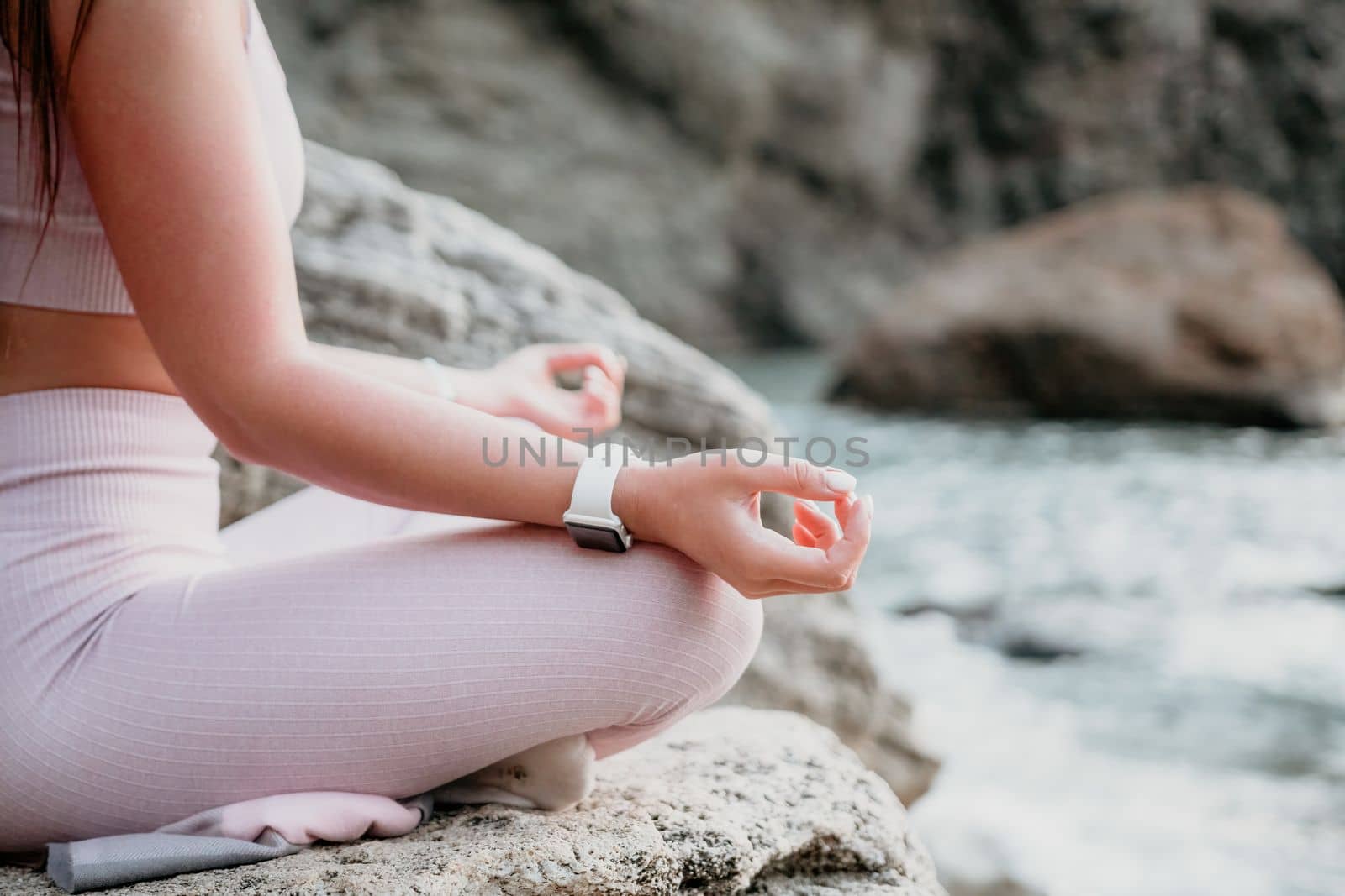 Young woman with black hair, fitness instructor in pink leggings and tops doing stretching and pilates on volcanic rocks near the sea on sunset. Female fitness yoga routine concept. Healthy lifestyle. by panophotograph