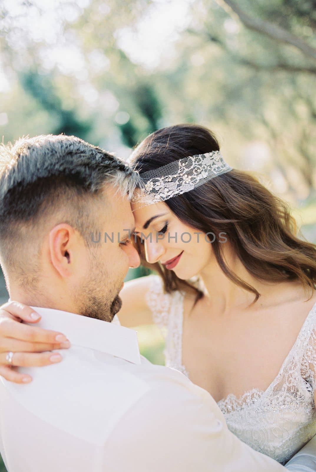 Groom touches his forehead to the forehead of bride, hugging her. Portrait. High quality photo