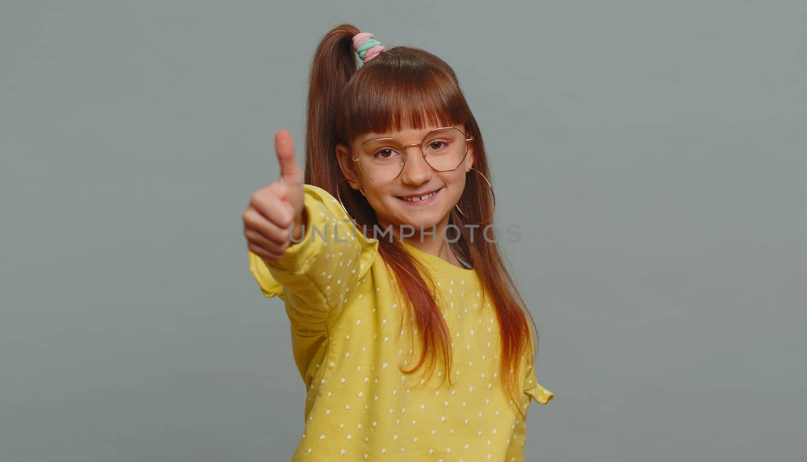 Like. Happy young preteen child girl kid looking approvingly at camera showing thumbs up, like sign positive something good, positive feedback. Toddler children isolated on studio gray background