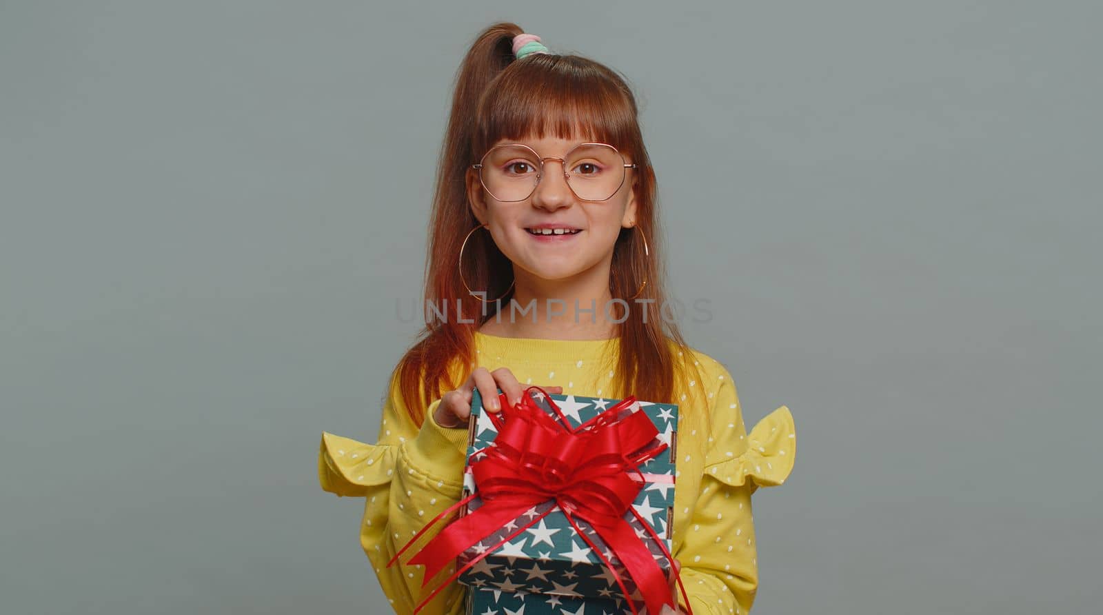 Happy toddler school girl receive, opening gift box and smiling joyfully, looking amazed satisfied with nice present unexpected birthday surprise. Teen female child kid isolated on gray background