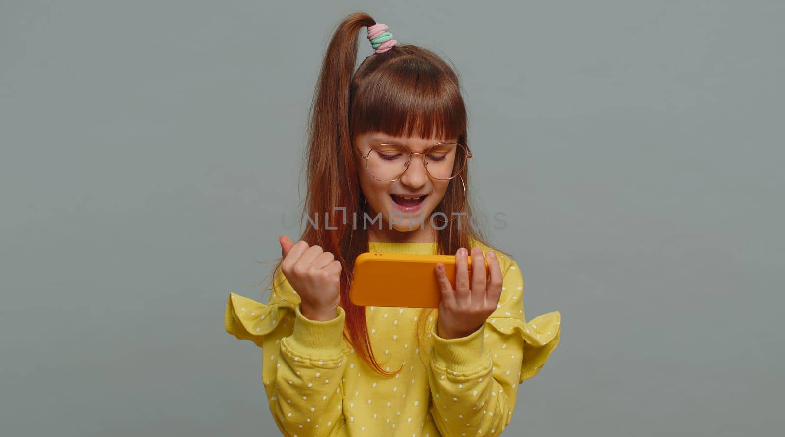 Worried funny young preteen child girl kid enthusiastically playing racing or shooter video games on smartphone. Excited little cute toddler children using mobile phone gadget app with drive simulator