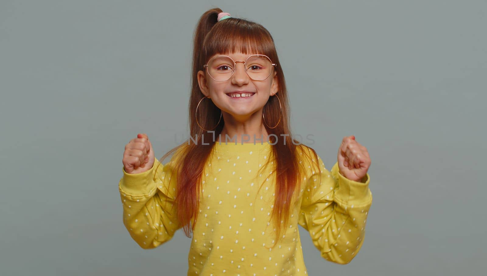 Young preteen child girl kid shouting, raising fists in gesture I did it, celebrating success, winning, birthday, lottery jackpot goal achievemen. Little toddler children isolated on gray background