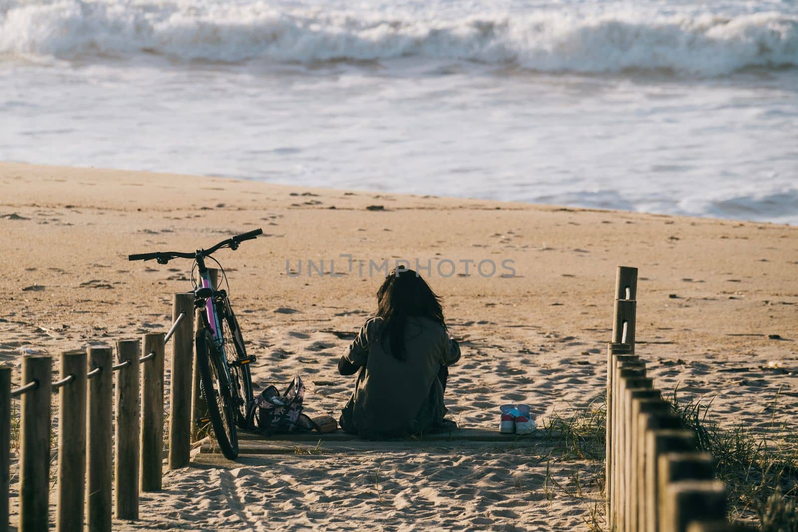 Girl alone with a bicycle sitting on the beach relaxed and calm in front of sea waves. by papatonic