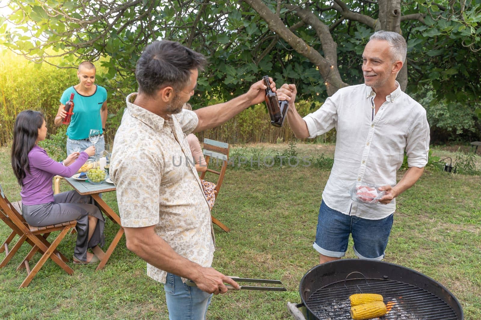 Group of friends toasting happy around the barbecue. Smiling people drinking on the patio. High quality photo
