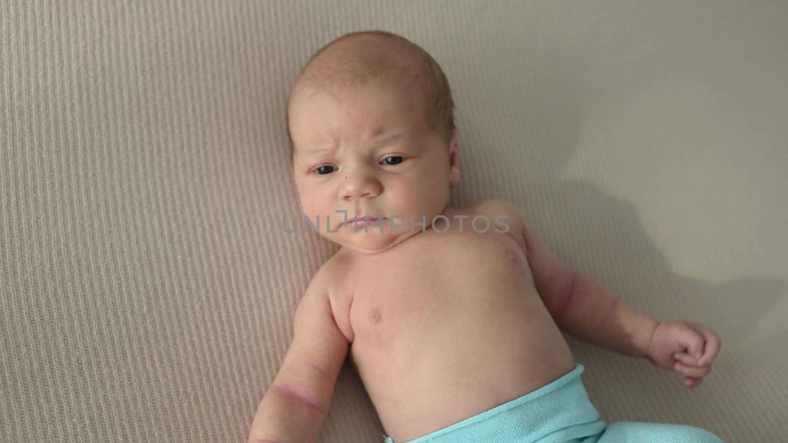 Newborn baby boy lying in bed and lloking around seriously. Infant child portrait at home