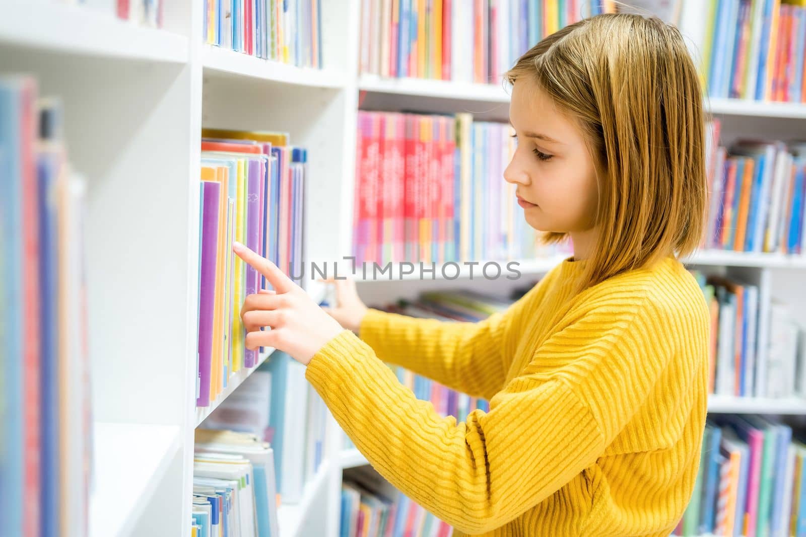 Schoolgirl choosing book in school library. Smart girl selecting literature for reading. Books on shelves in bookstore. Learning from books. School education. Benefits of everyday reading