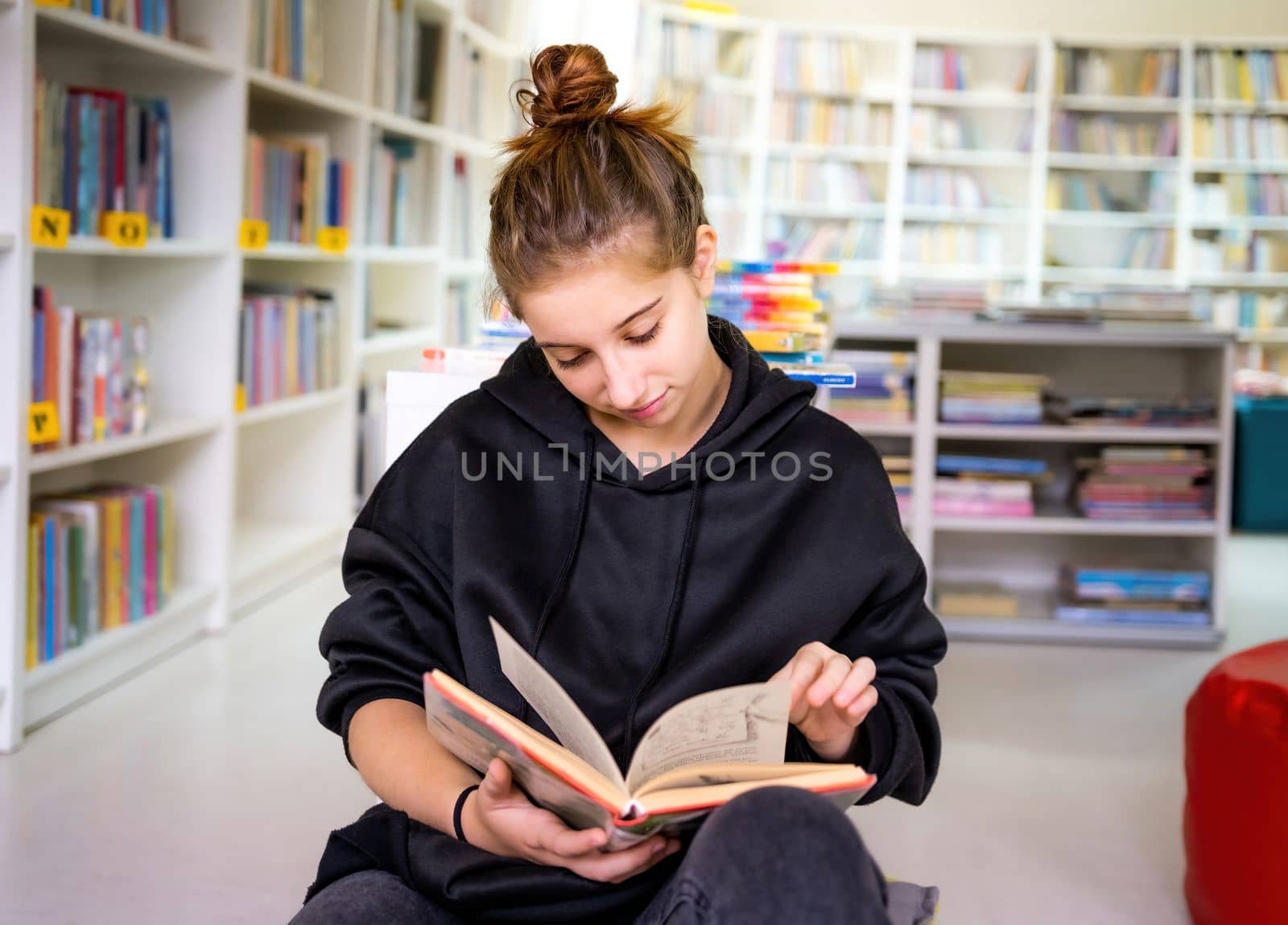 Student reading book in library leaning against bookshelves at the university
