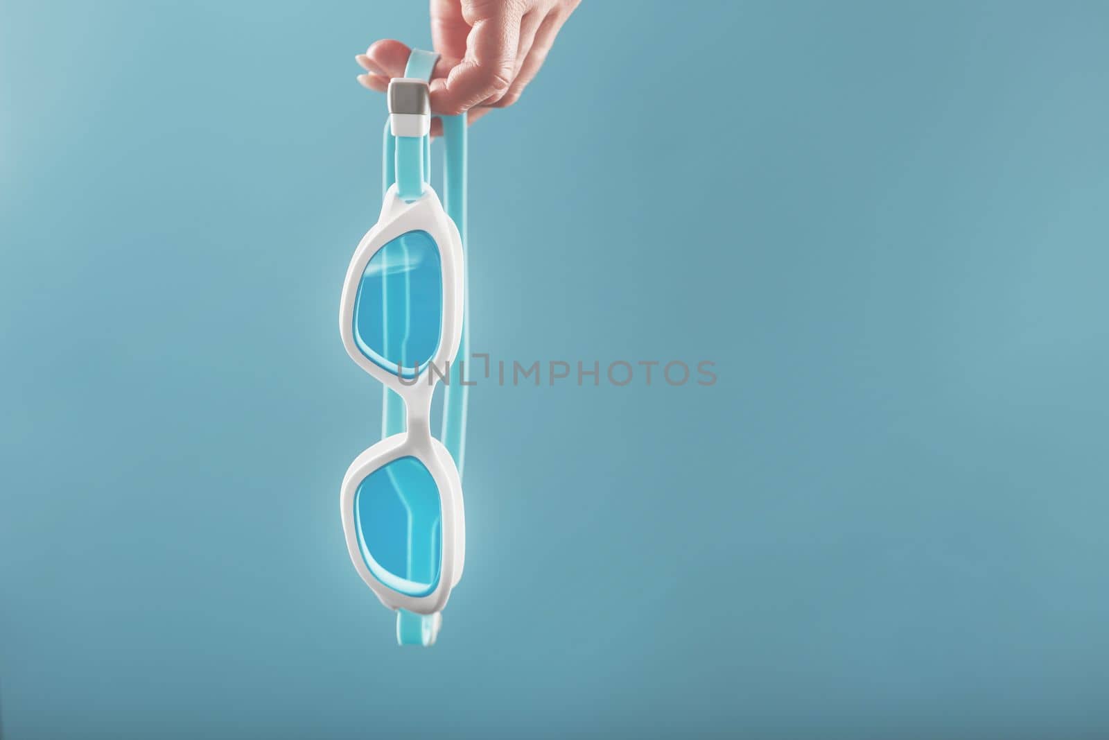 White swimming glasses in hand with a blue lens on a blue background by AlexGrec