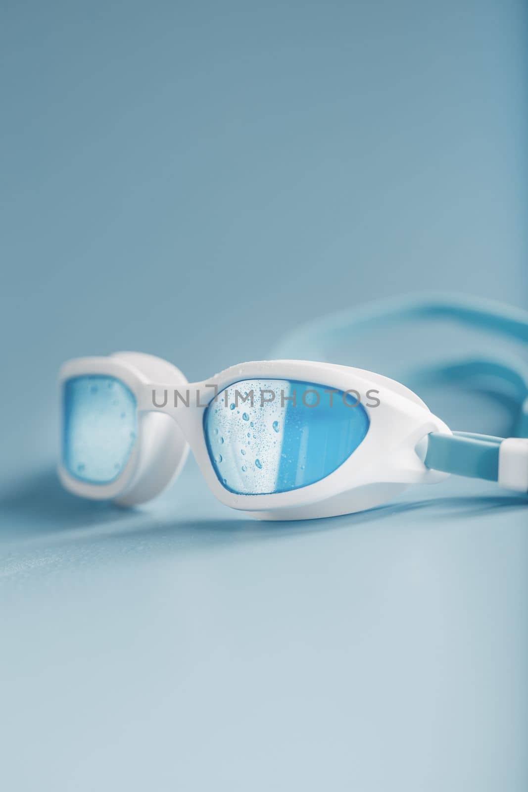 White swimming glasses with a blue lens on a blue background