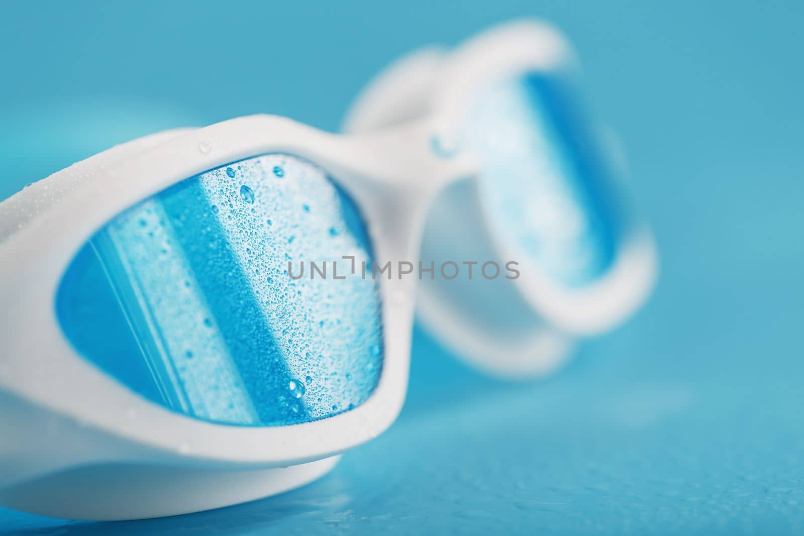 White swimming glasses with a blue lens on a blue background