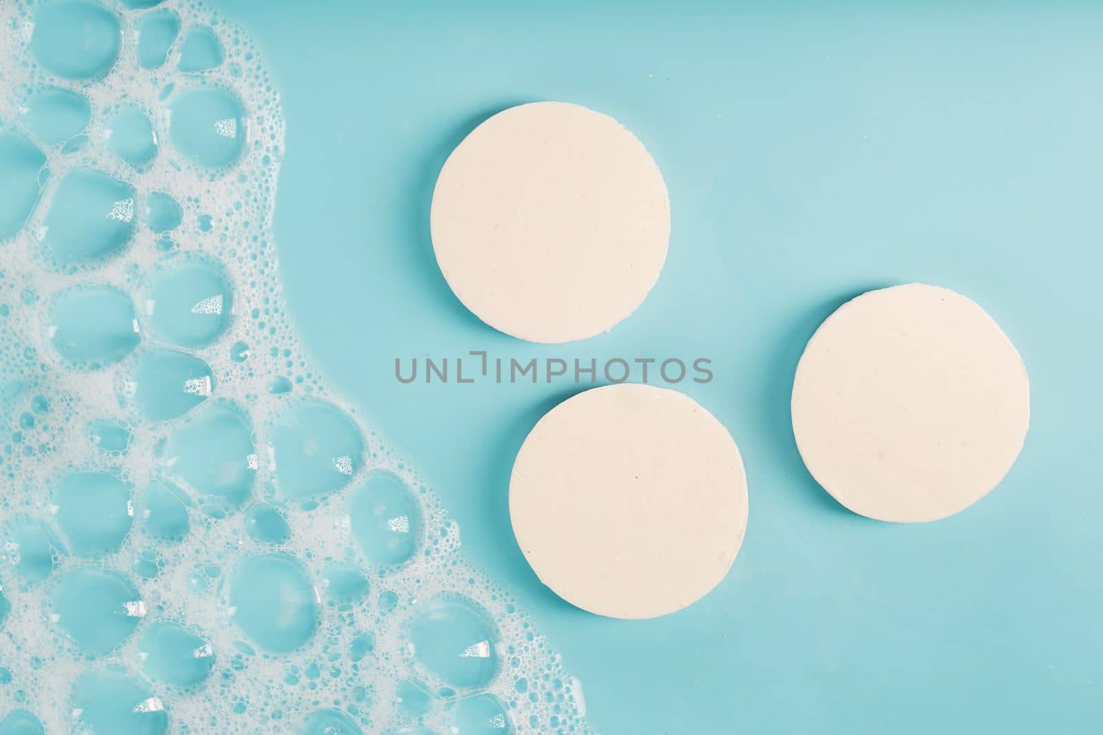 Three round pieces of white soap with foam on a blue background