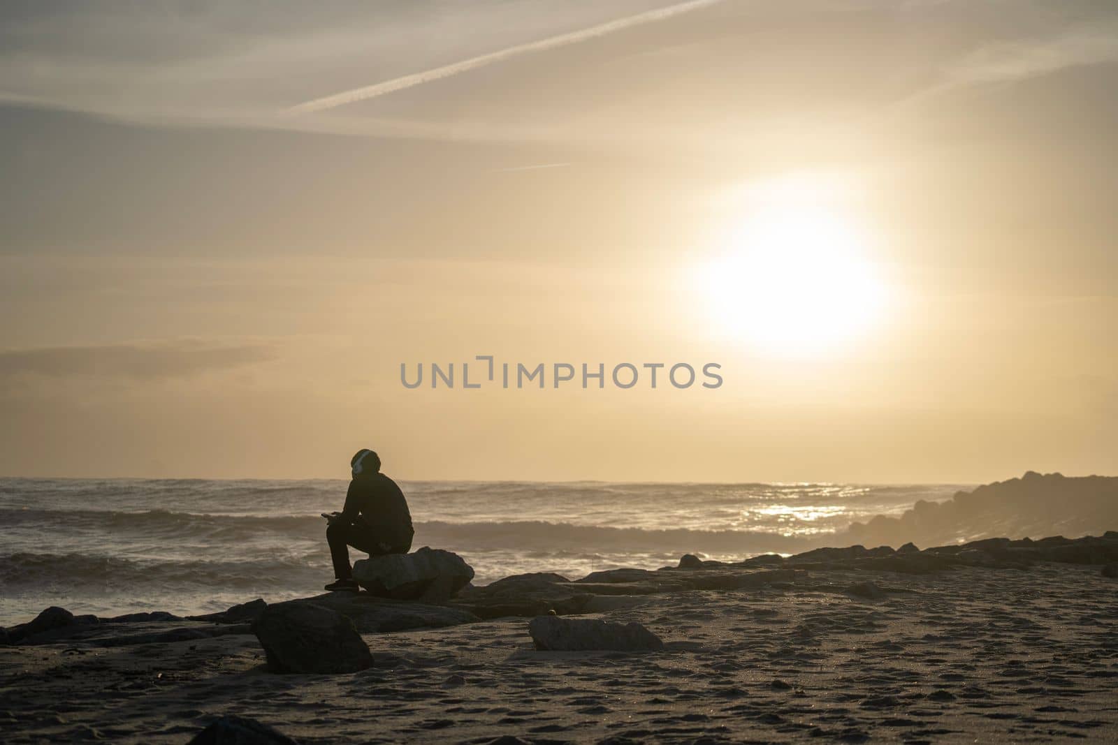 Silhouette of boy sitting with headphones on the seashore beach at sunset time. Handsome Asia man model in his 20s