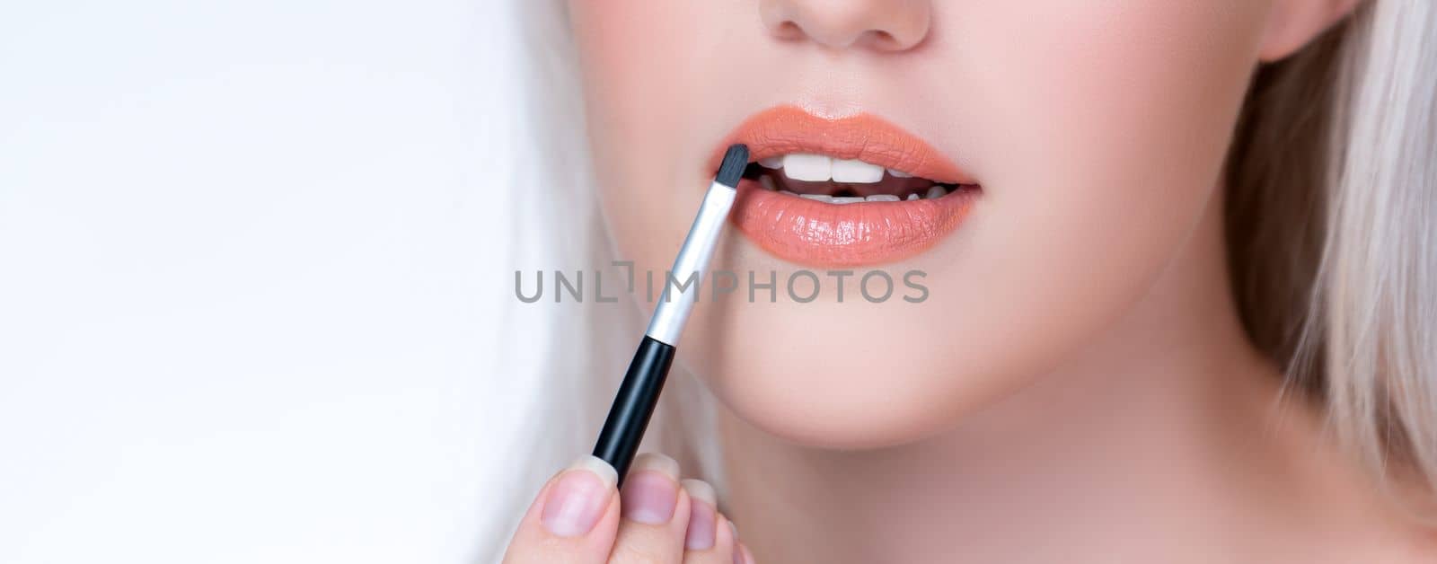 Closeup personable young woman putting alluring fashion glossy lipstick. by biancoblue