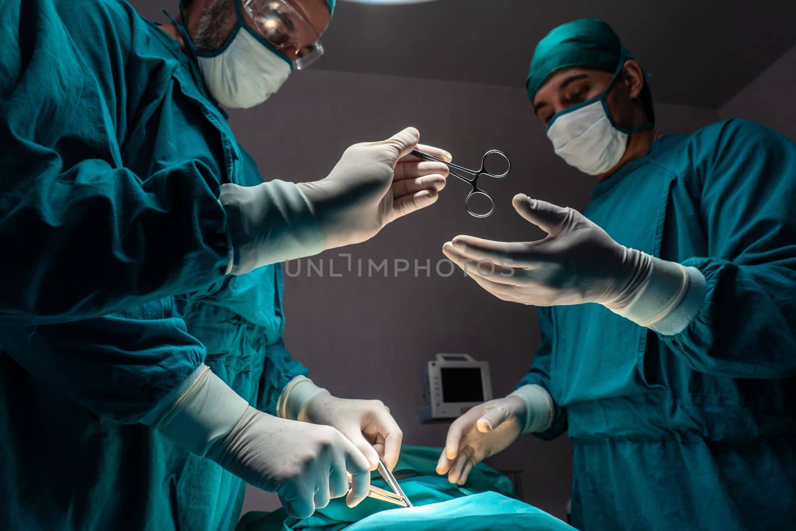 Surgical team performing surgery to patient in sterile operating room. In a surgery room lit by a lamp, a professional and confident surgical team provides medical care to an unconscious patient.