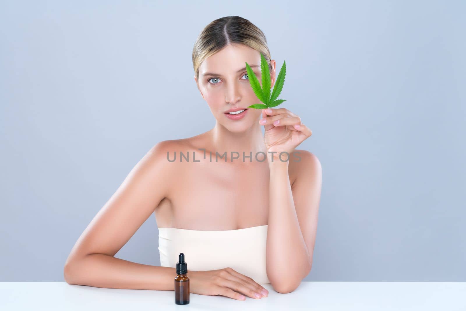 Alluring portrait of beautiful woman in isolated holding green leaf with marijuan extracted bottle for skincare treatment product. Cannabis CBD oil for cosmetology and beauty concept.