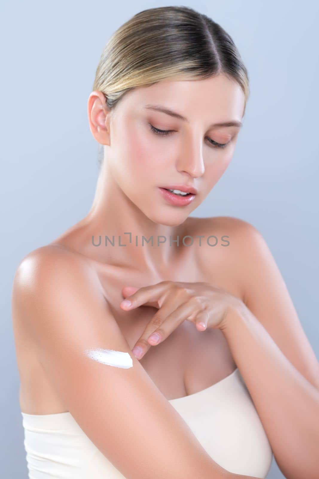 Alluring beautiful woman applying moisturizer cream on her arm for perfect skincare treatment in isolated background. Caucasian women portrait with skin rejuvenation and cosmetology concept.