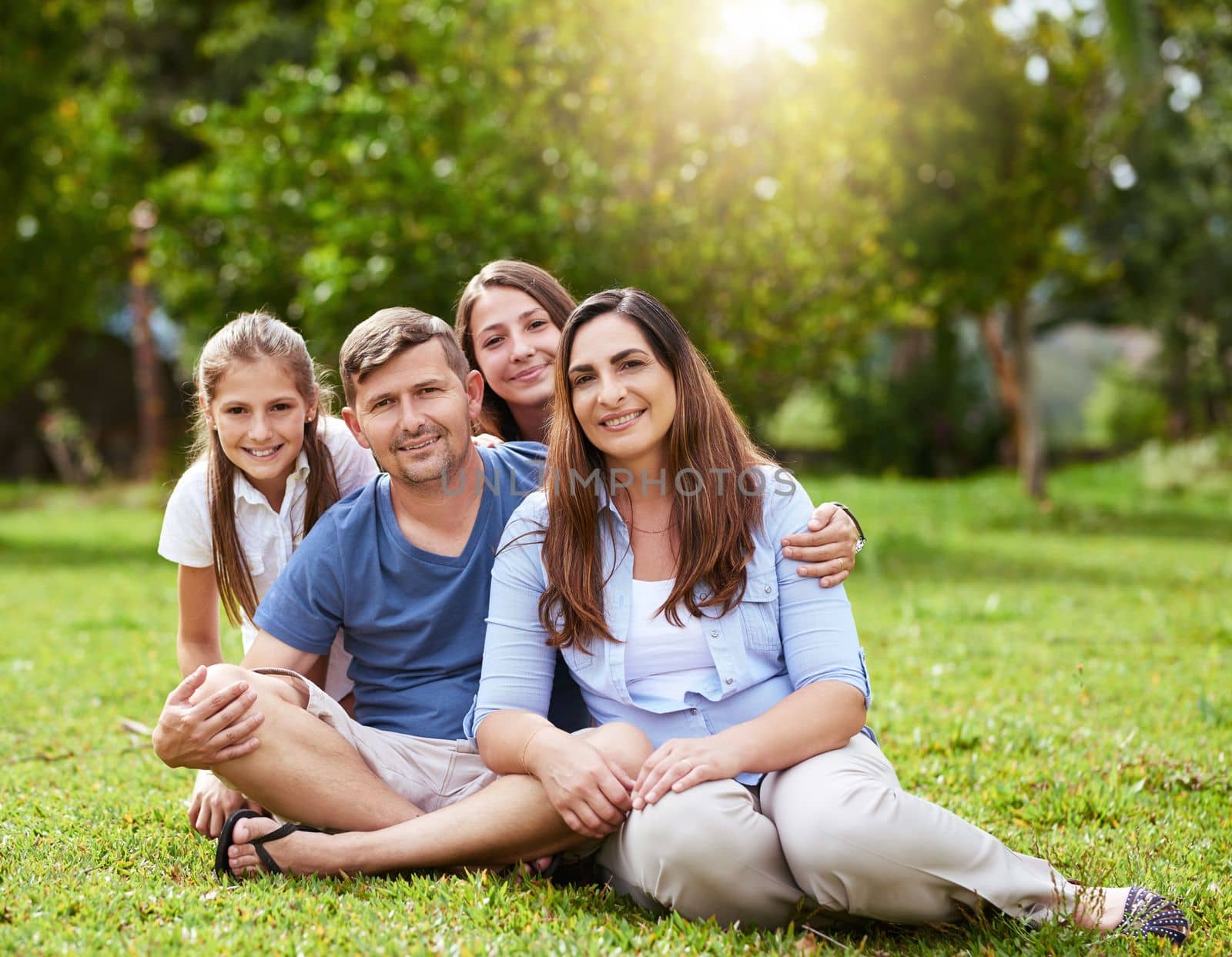 Family is all you need. Portrait of a cheerful young family seated in a park together outside during the day. by YuriArcurs