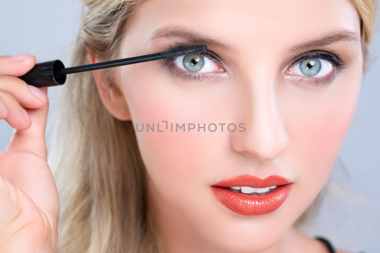 Closeup woman with blond hair putting alluring black mascara with brush in hand on long thick eyelash. Perfect fashionable cosmetic clean facial skin with beautiful eye young woman in high resolution.
