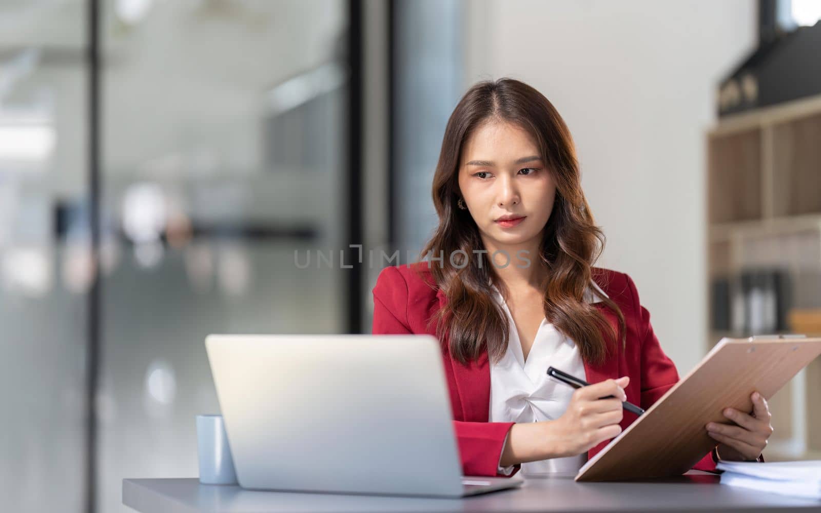 Young Asian businesswoman sitting at their desk and take notes using laptop in the office by nateemee